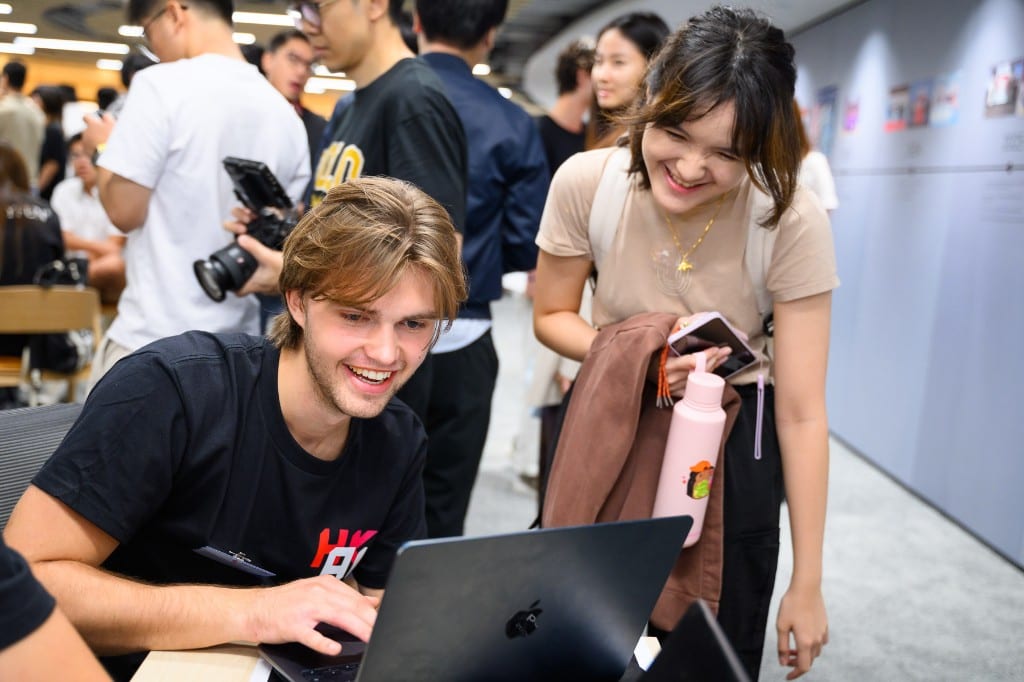 Finley Sieben working on a laptop during the Hong Kong AI Summit, a teammate looking on