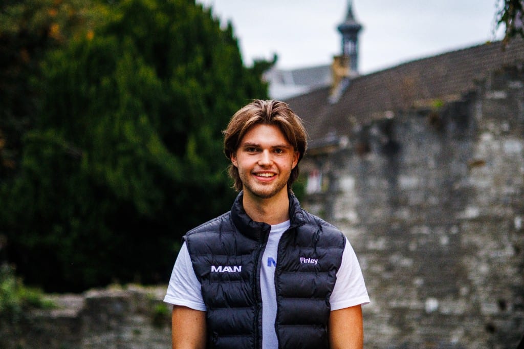 Finley Sieben outdoors in a MAIN vest, with historic stone buildings behind him